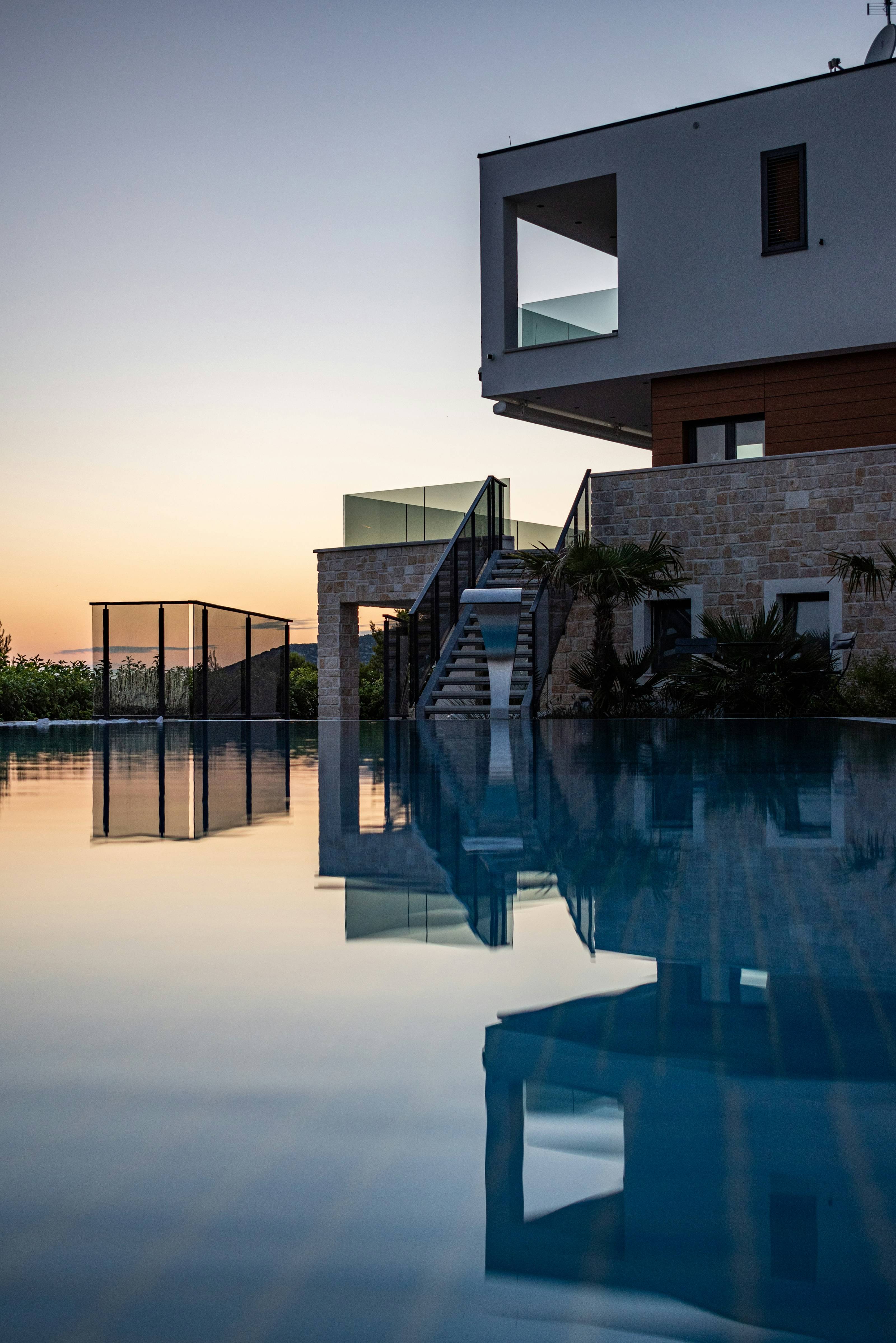 Casa de pedra e vidro com piscina de borda infinita refletindo o céu ao entardecer
