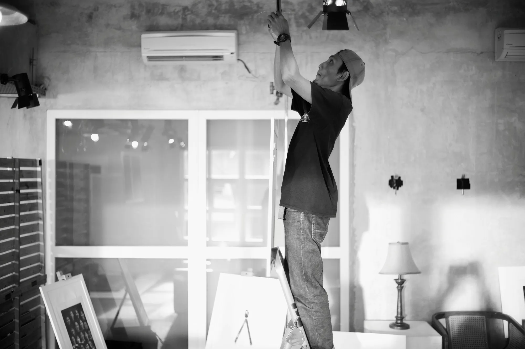 Técnico em uma escada trabalhando na instalação elétrica de um ambiente com ar-condicionado na parede